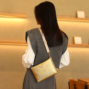 Golden crossbody bag with chevron pattern and adjustable strap on a female model