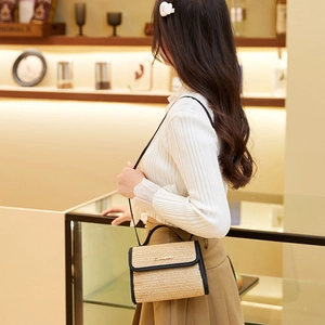 Straw woven crossbody bag with black leather trim and gold metal logo displayed by model