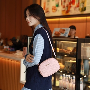 Sac bandoulière rose matelassé avec broderie en V et logo doré porté par un mannequin