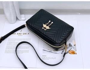 Detail of black chevron quilted camera bag with golden wing buckle and wave edge strap