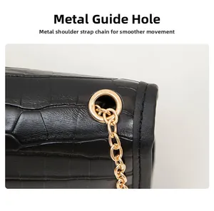 Detail of golden metal eyelets and chain strap on a black crocodile texture handbag
