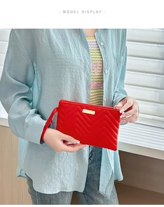 Detail of red quilted PU clutch bag with golden metal decor and wristlet strap on a model