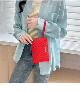 Detail of red quilted wave pattern clutch bag with gold metal plate and wrist strap