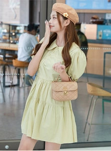 Detail of beige quilted mini bag with gold clasp paired with light green dress
