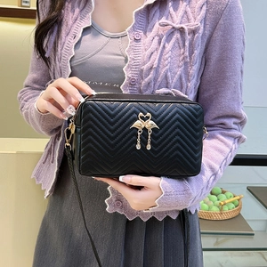 Sac bandoulière matelassé noir avec logo cygne doré porté par un mannequin femme
