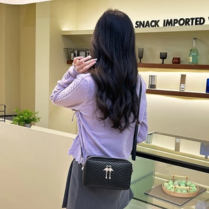 Sac bandoulière noir matelassé avec boucle cygne dorée et pompon porté par un mannequin