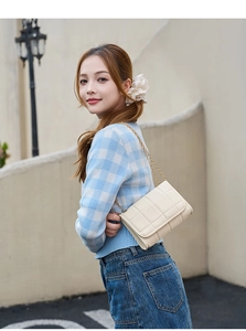 Outdoor shot of a beige quilted chain bag with a gold metal strap and flap design