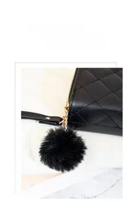 Détail du pompon noir duveteux avec chaîne dorée sur un portefeuille matelassé