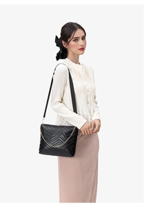 Detail of black wave quilted bucket bag showing chain decor and wide strap on model