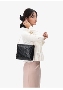 Detail of black quilted bucket bag featuring wave stitching and gold chain strap