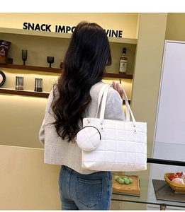 Rear view of a model carrying a white quilted tote bag with a small round pouch accessory