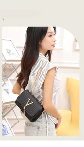 Detail shot of black crossbody bag with metallic V logo, tassel, and gold chain strap