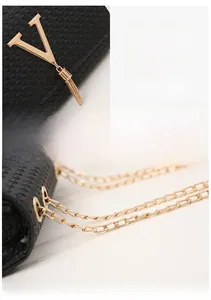 Detail of black woven texture bag featuring golden V-shaped buckle and fringe accent