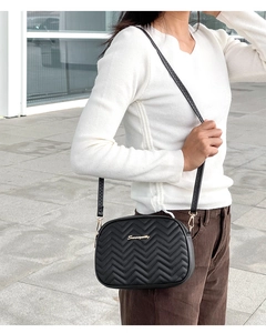 Detailed shot of black chevron quilted crossbody bag with gold logo and adjustable strap