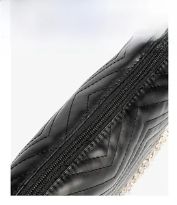 Detail of black chevron quilted leather cross-body bag with golden chain and zipper closure