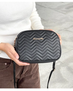 Detail of black wave quilted crossbody bag with gold logo held against city background
