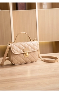 Close-up of a beige quilted handbag with gold hardware on a warm wooden surface