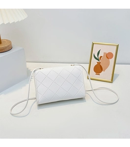 Detailed view of white quilted crossbody bag with rhombic stitching on a modern desk