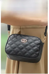 Detail of a black quilted crossbody bag with golden hardware on a lady's shoulder