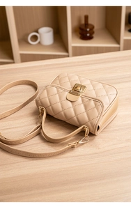 Detail of beige quilted handbag with golden twist lock and thin wavy shoulder strap