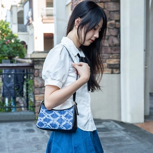 Blue denim patterned shoulder bag with black strap worn by a model in outdoor setting
