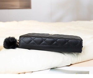 Détail de la pochette noire matelassée avec pompon en peluche et zip doré