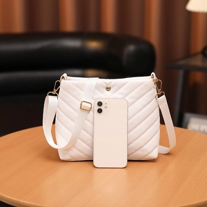 White chevron quilted bucket bag with golden hardware and wide fabric strap and phone for scale