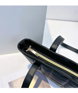 Gros plan sur la fermeture éclair dorée et le motif matelassé du sac cabas noir