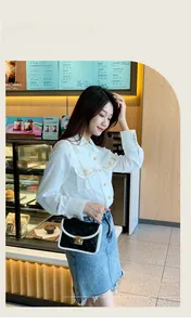 Detail of black quilted shoulder bag with white trim and gold lock in a cafe setting
