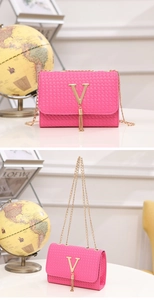 Close-up of fuchsia woven crossbody bag featuring a gold V-logo and fringe tassel detail