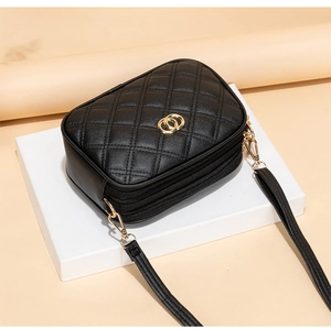 Detail of black quilted crossbody bag featuring dual gold zippers and smooth PU leather