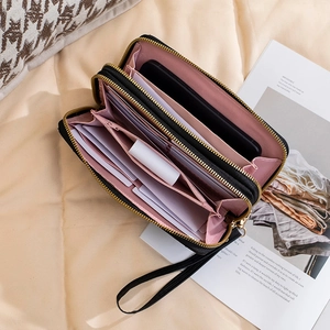 Chic black double zipper wallet with pink lining and wristlet strap on beige fabric
