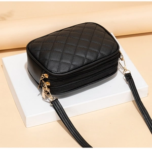 Close-up of black quilted crossbody bag with three zipper sections and gold hardware