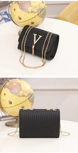 Detail of black woven texture bag with gold V-shape hardware and delicate tassel pendant