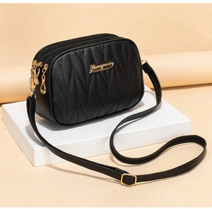 Detail of black quilted crossbody bag showing three zippers and golden hardware logo