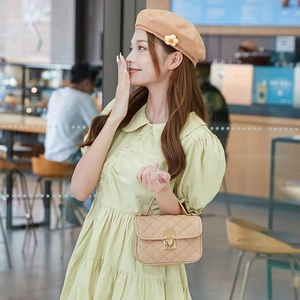 Sac à main beige matelassé avec fermoir métal porté par femme en robe vert clair