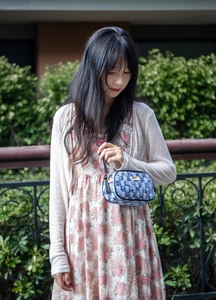 Detail of blue checkerboard crossbody bag with gold hardware worn over floral dress