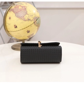 Close-up of woven texture black crossbody bag with gold tassel lock and buckle