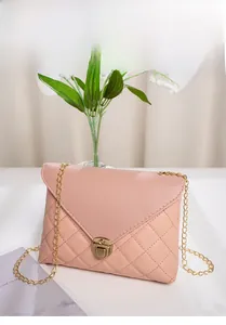 Detail of pink quilted handbag with gold chain strap and twist-lock on white surface