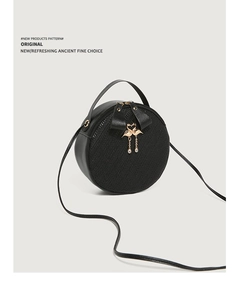 Detail of round black crossbody bag featuring woven texture and gold swan charm tassel