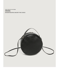 Detail of a minimalist black circular crossbody bag with smooth faux leather and top handle