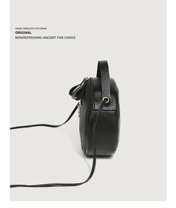 Detail view of the side profile on a black circular crossbody bag with litchi grain texture
