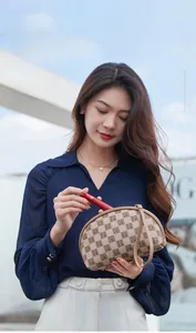 Putting lipstick into shell-shaped cosmetic bag with brown monogram pattern texture