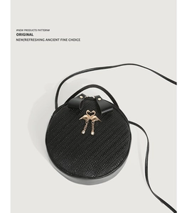 Detail of black woven texture round crossbody bag with golden flamingo clasp and bow