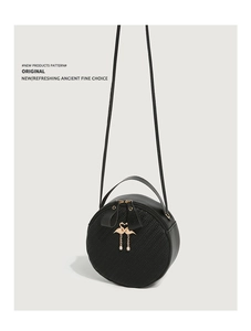 Detail of black round crossbody bag with woven texture, flamingo charm and pearl accents