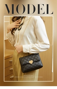 Detail shot of black quilted shoulder bag featuring gold heart lock and chain strap
