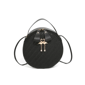 Black round woven crossbody bag with dual zippers and golden swan pendant accessory
