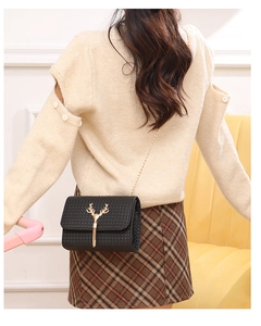 Detail of black woven crossbody bag featuring golden deer antler clasp and tassel on model