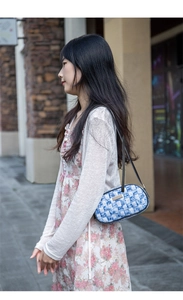 Outdoor lifestyle shot of a woven blue and white underarm bag with gold metal plaque