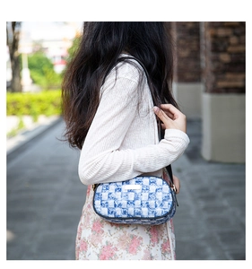 Detail of floral checkered denim shoulder bag with golden metal plaque and slim black strap